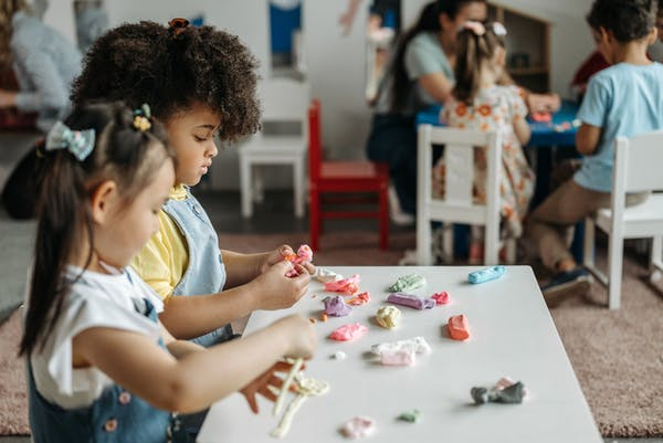 Two children seated next to each other playing with moulding clay