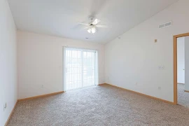 Living room with carpeted flooring, patio doors with vertical blinds, ceiling fan, white walls, and wood trim 