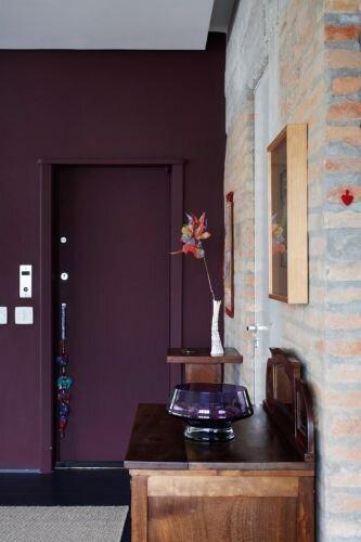 Ambiente com porta e parede roxa, móvel de madeira com vaso.