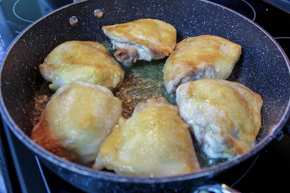 Chicken thighs cooking in a skillet.