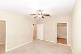 Carpeted bedroom with a walk-in closet and door to the private bathroom with a ceiling fan overhead