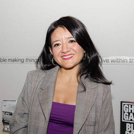 Image of Erika Soto-Lamb wearing gold hoop earrings, purple top and a check blazer.