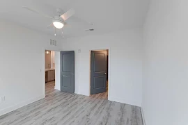 Bedroom with light grey wood floors, dark grey doors, & white walls & trim. White ceiling fan with covered dome lighting