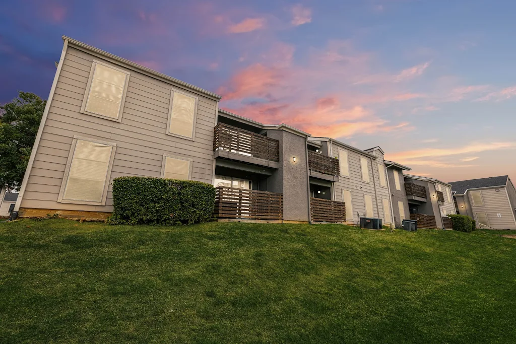 Apartment complex with neutral siding and stucco behind a grassy area at dusk.