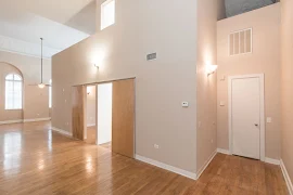 Entry way with wood flooring, tall ceilings, two wall mounted lights, beige walls and white trim