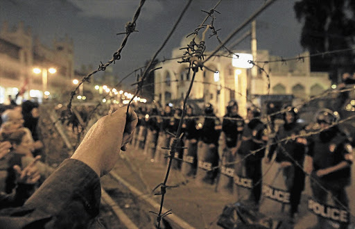 LINE IN THE SAND: Anti-Morsi protesters in front of the presidential palace in Cairo on Tuesday. Egyptian police battled thousands of protesters outside President Mohamed Morsi's palace, prompting the Islamist leader to leave the building Picture: MOHAMED ABD EL GHANY/REUTERS