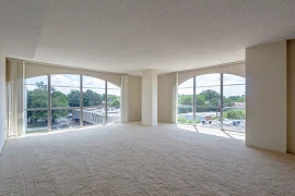 Living room with two floor to ceiling windows with neutral colored walls and carpet