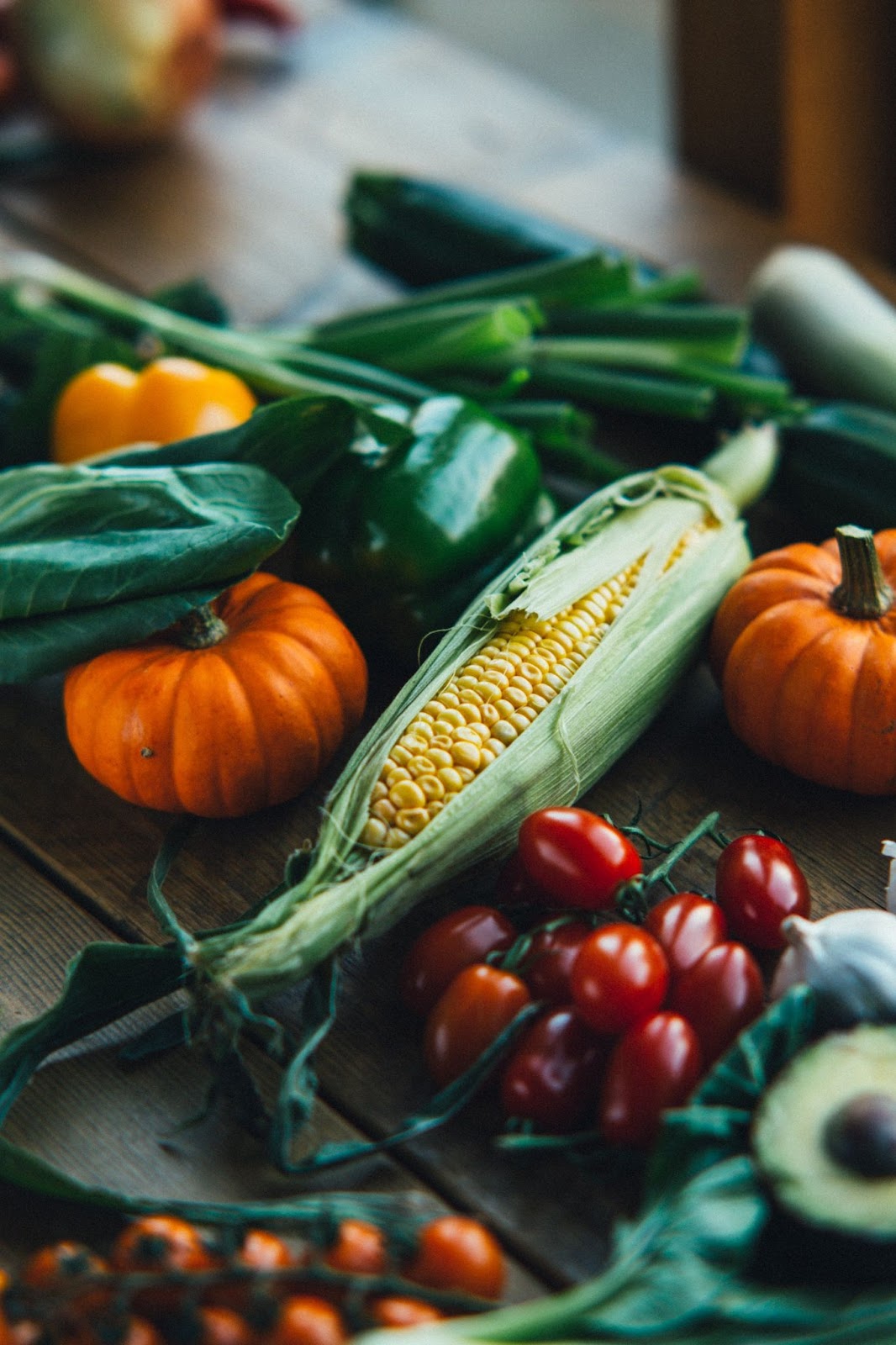 green leafy vegetables, corn, peppers, squash and many more are on a table