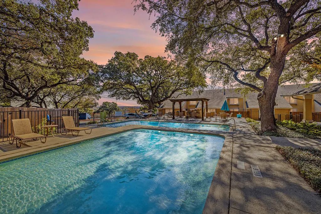 The Arbors at Tallwood's two swimming pools at dusk with sundeck featuring lounge chairs and several trees surrounding