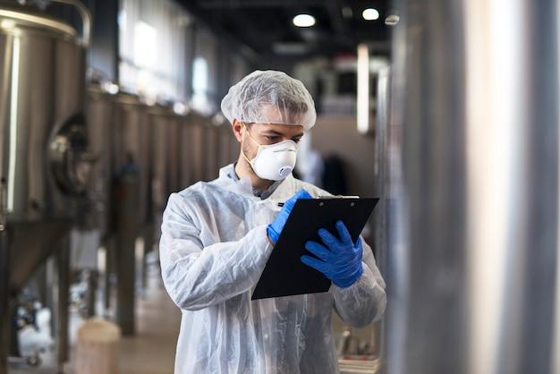 Foto grátis tecnólogo em uniforme branco verificando qualidade em fábrica de produção industrial