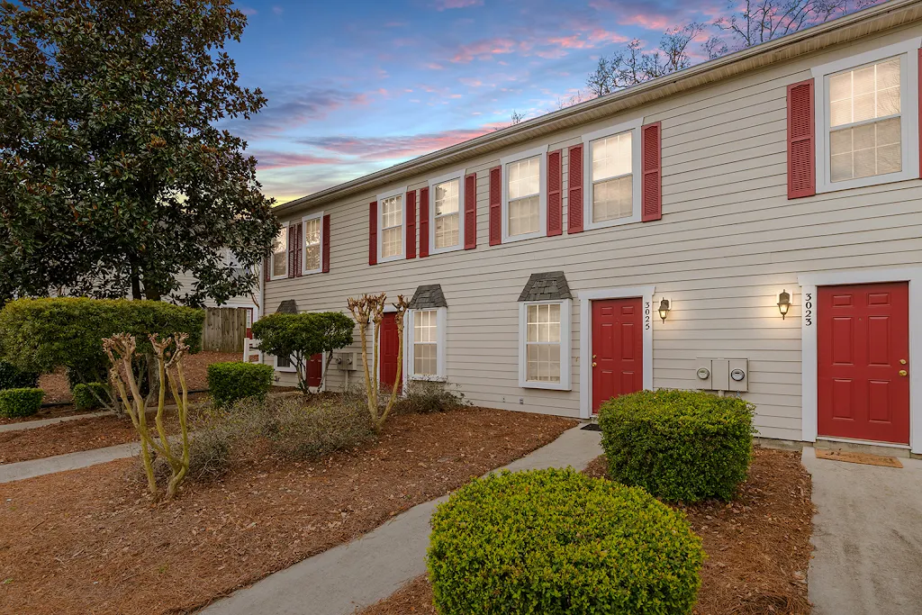 Apartment building with light siding and red accents at dusk