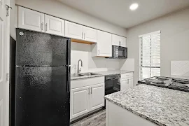 Modern kitchen with white cabinets, black appliances, and gray granite countertop in a bright apartment.