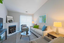 Model living room with light walls, high ceilings, fireplace with mantle and mirror above, plush couch, and a coffee table