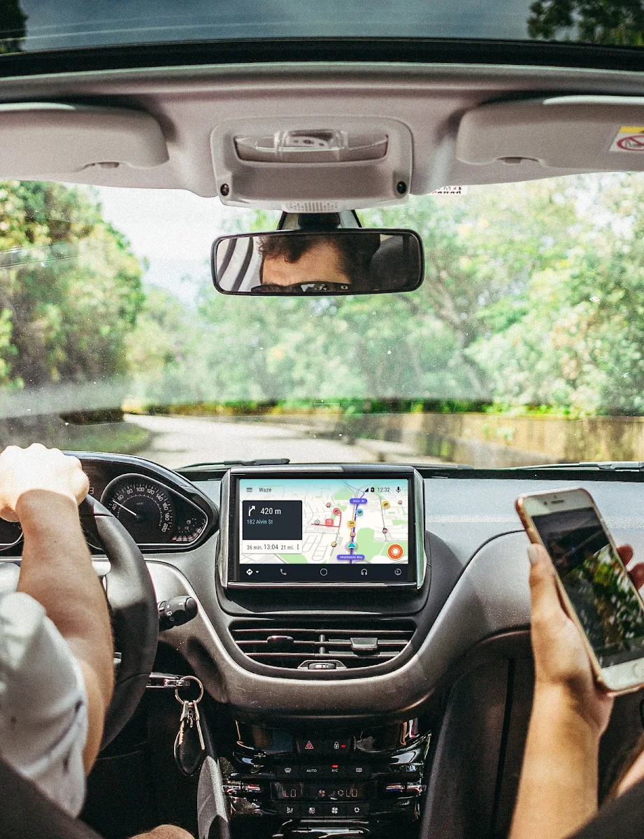 Blick auf ein Armaturenbrett vom Rücksitz aus. Zu sehen sind ein Display mit Waze und eine Hand in 2-Uhr-Position am Lenkrad.