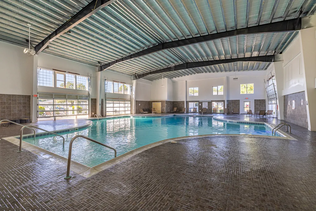 Indoor community pool with garage doors to outdoor seating area, metal ceilings, and lounge chairs surrounding