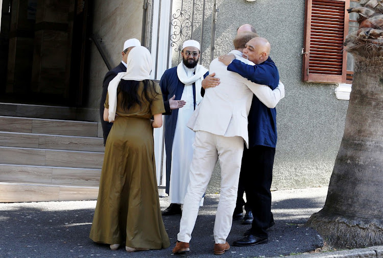 Prince Harry hugs Michael Weeder, dean of St George's Cathedral, while Meghan Markle chats to Muslim community leader Mohamed Groenwald, left, and Sheikh Ismail Londt, imam of the Auwal Mosque in the Bo-Kaap, Cape Town. The Duke and Duchess of Sussex visited the city's oldest mosque on Heritage Day, September 24 2019.