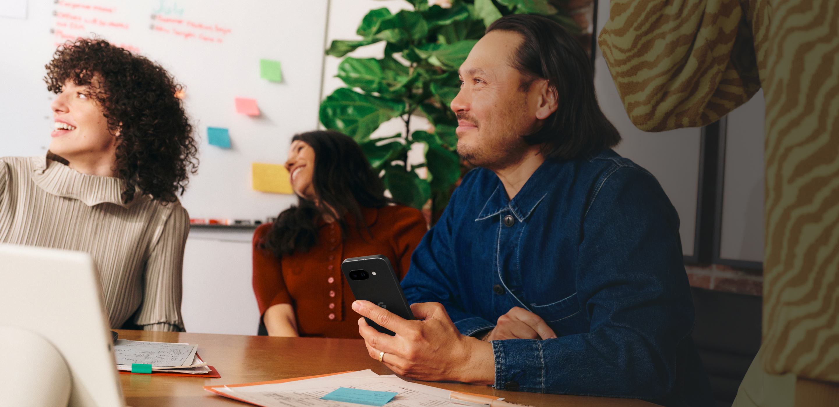 A small business owner using his Google Pixel 9a phone during a meeting with his team.