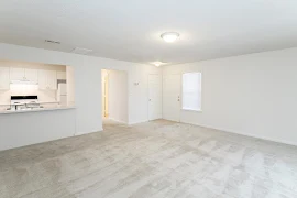 Living room with light carpet and walls, Front door, storage closet, window with blinds, hallway, and view of kitchen