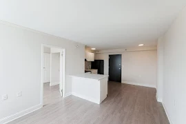 Living room with wood-inspired flooring, light walls and trim, entryway door to bedroom, and access to the kitchen area