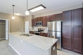 Kitchen with large island, light speckled granite countertops, stainless steel appliances, and dark cherry wood cabinets