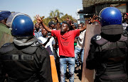 A supporter of the Movement for Democratic Change (MDC) opposition party of Nelson Chamisa gestures to the riot police as they march on the streets of Harare, Zimbabwe.