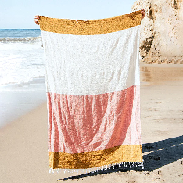 photo of a throw blanket with yellow, white, and pink stripes with a beach in the background