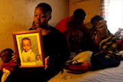 Tshidi holds a photo of Tinyiko Reckson Mongwe who was killed, while his mother, Rosina Mosiuoa, is comforted by her siblings at the back. Photo: SANDILE NDLOVU