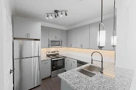 Kitchen with stainless steel appliances, stone speckled gray countertops, tile backsplash, and gray cabinets