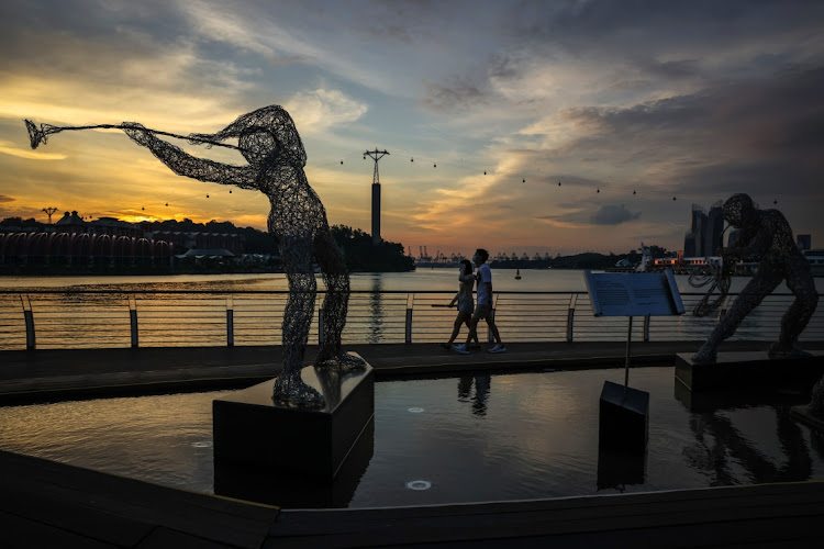 Pedestrians wearing protective face masks, mandated to be worn at all times outside, walk along a promenade on December 23, 2020 in Singapore.