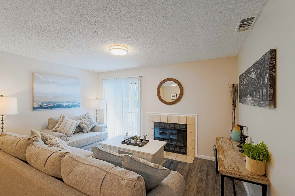 Model living room with plush couches, wood-inspired flooring, fireplace with tile surrounding, and decorative accents