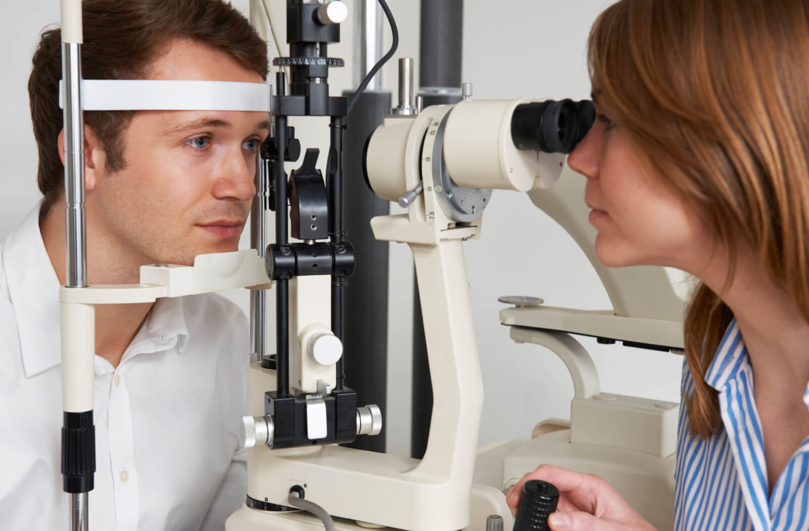 A female optometrist examining the eyes of a young  man using a medical device to detect potential eye problems.
