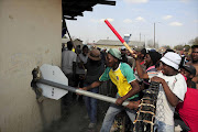 Community members trying to bring down a wall to get access to a foreign owned shop as they protest for land and housing. Photo Thulani Mbele