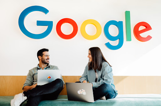 Two Googlers smiling and staring at each other. Google logo in the background.