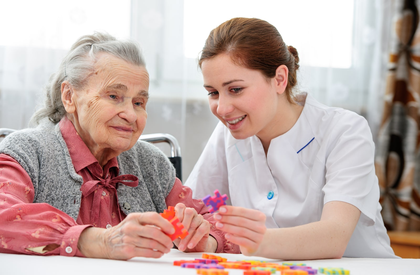 A female nurse helping a memory care patient with a puzzle