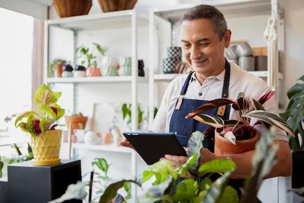 A garden store employee behind a counter with a counter with a tablet in his hand.