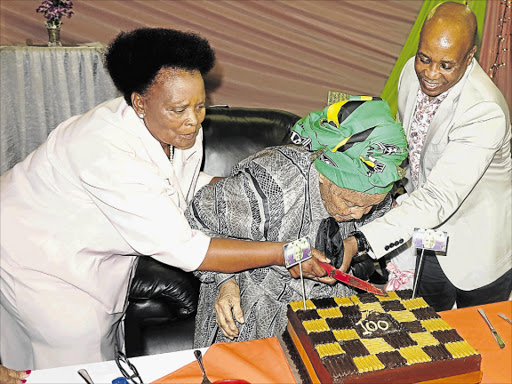 SWEET MOMENT: Centenarian Mama Noyose Mabel Gija is helped by her daughter Sheila Qambela, 66, and surprise guest Eastern Cape premier Phumulo Masualle, as she cuts her chocolate birthday cake Picture: MBALI TANANA