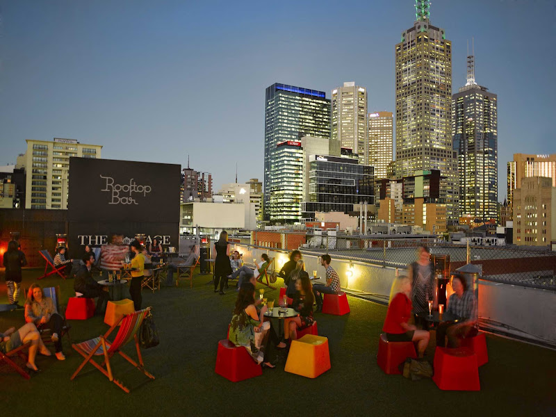 People enjoy drinks at the Rooftop Bar & Cinema at Curtin House at twilight in Melbourne.