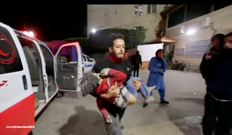 A member of the Palestine Red Crescent Society carries a Palestinian child as wounded Palestinians are rushed into a hospital following Israeli strikes, amid the ongoing war between Israel and the Palestinian Islamist group Hamas, at a location given as Deir al-Balah, Picture: PALESTINE RED CRESCENT SOCIETY via REUTERS