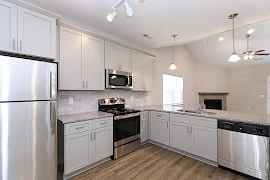 Back wall of kitchen has stove and overhead microwave between cabinets and granite countertops with the refrigerator to left