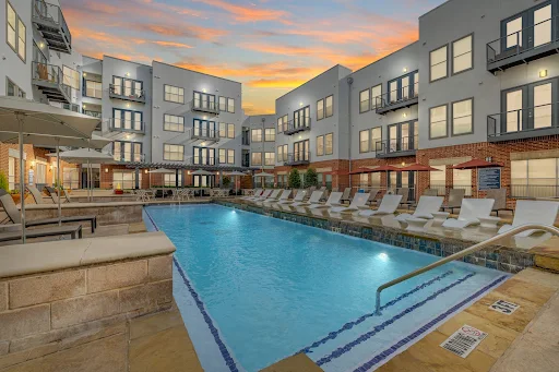 Apartment complex featuring a swimming pool surrounded by lounge chairs and outdoor seating areas at dusk