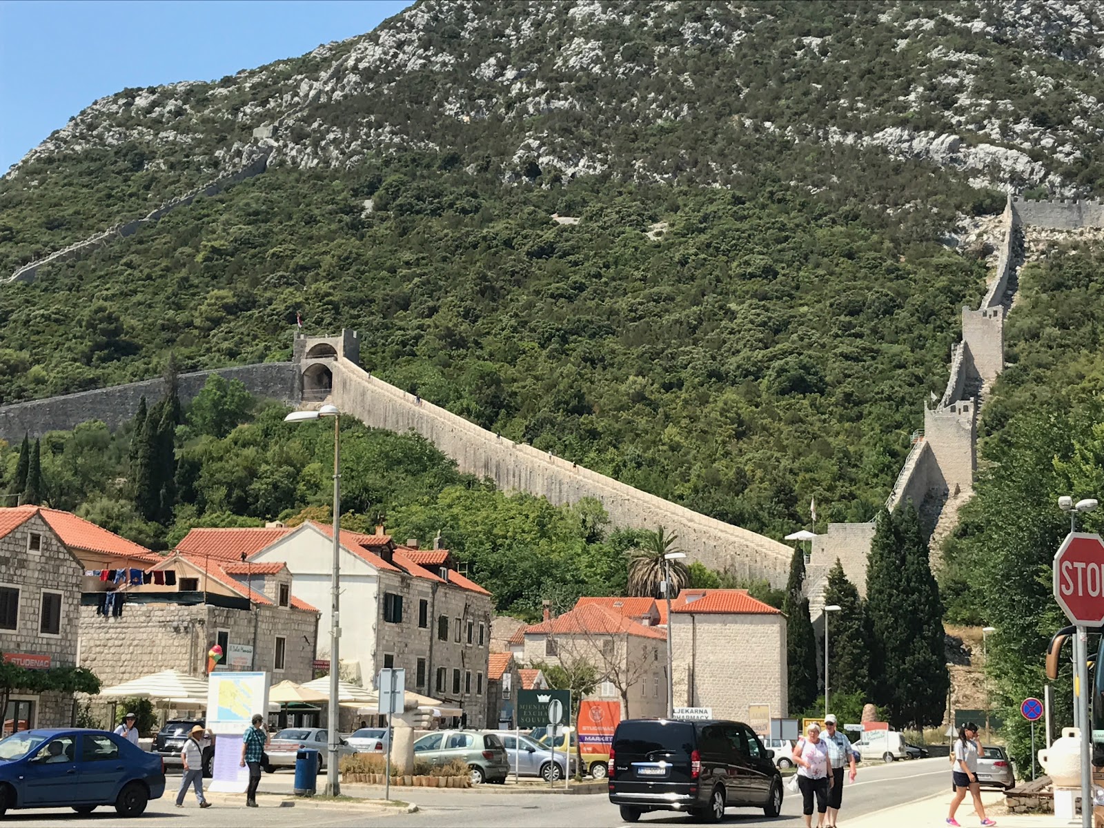 the great walls of ston. medieval defense walls on a green hill, with traditional croatian buildings and tourists in the foreground. sunny day in ston, croatia.