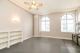 Living room area with shelves, two large arched windows and horizontal blinds. Light gray walls with white trim