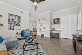 Modern apartment living room with grey sofa, glass coffee table, white built-ins, and decorative art on walls.