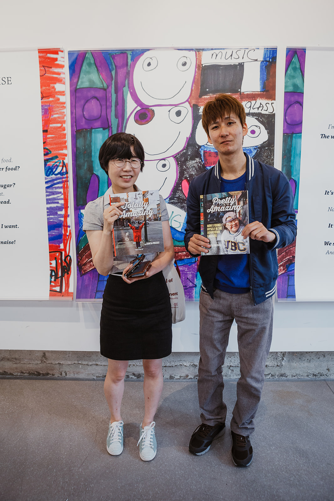 Two international visitors hold copies of Teresa's 'Amazing' books as they pose for a photo. Teresa's 'Wind Warning' artwork hangs in the background. Photo: This Is It Studios.
