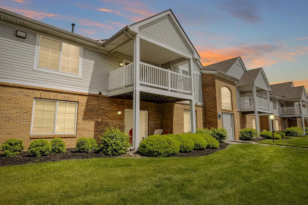 Twilight view of a multi-unit brick apartment complex with white balconies, manicured lawn, and a clear sky background.