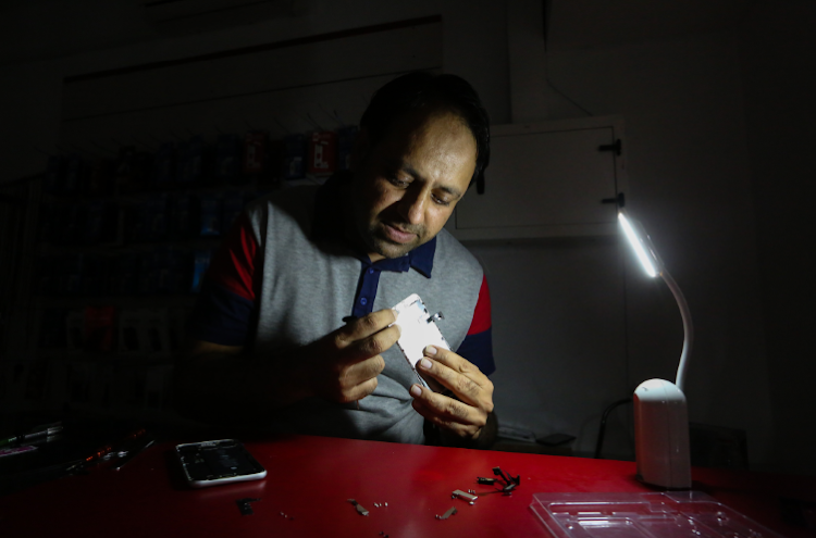 Muhammad Zubair tries to fix a clients cell phone during load shedding at Mahi Cellular in 6th Ave shopping centre.