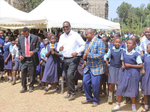 Governor Evans Kidero (centre), Roysambu MP Ndirangu Waihenya (right), and Roysambu MCA Peter Warutere join pupils for a dance at Garden Estate Secondary School on Tuesday, March 14, 2017. /JULIUS OTIENO