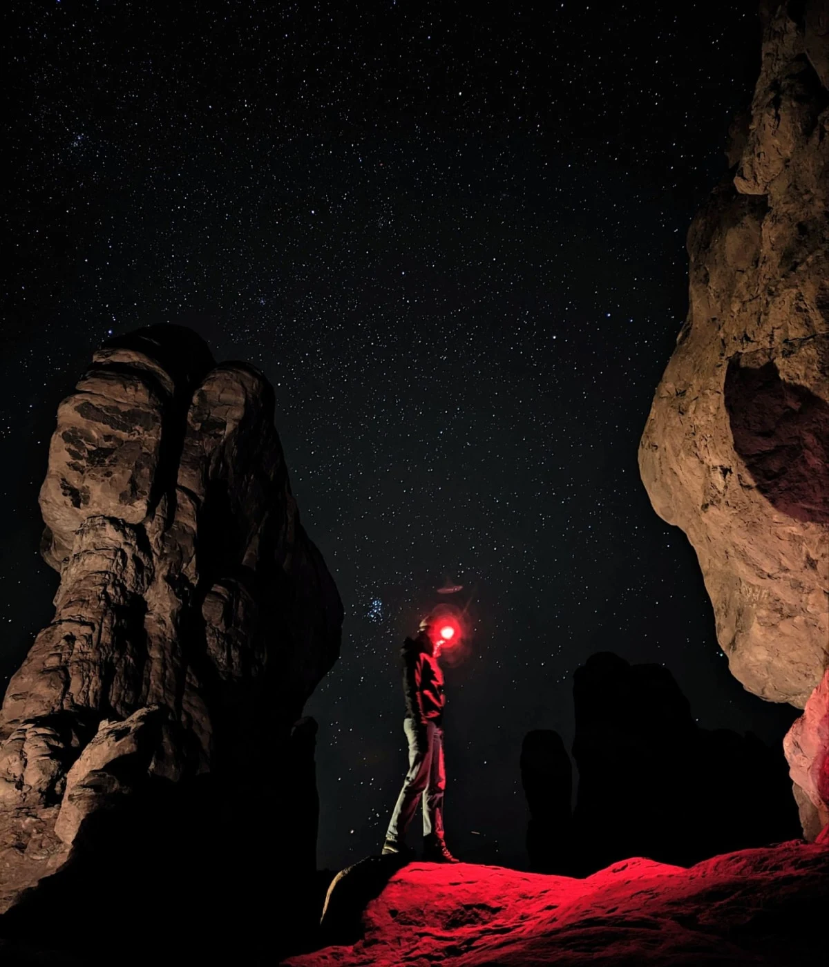 Una foto di una persona in piedi tra le rocce rosse di notte. Nonostante le condizioni di scarsa illuminazione, la foto contiene dettagli brillanti.