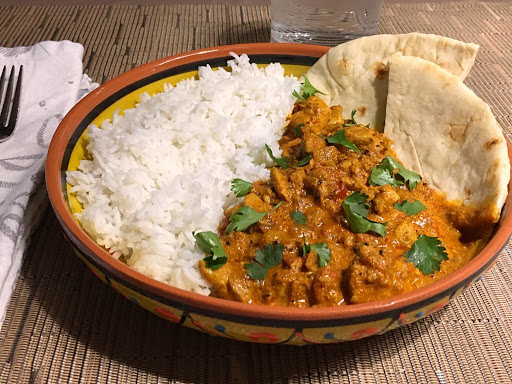 A chicken dish served in a bowl with rice and naan bread.