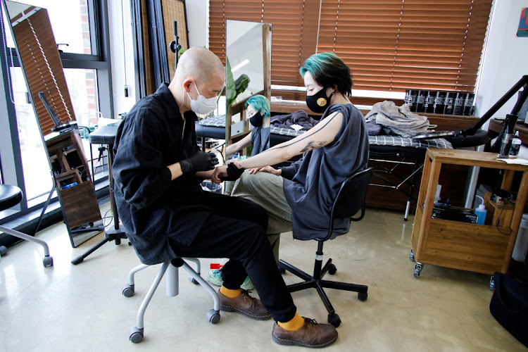 Tattooist Kim Do-yoon attends to a customer in his tattoo studio in Seoul, South Korea, February 15 2022. Picture: REUTERS/HEO RAN